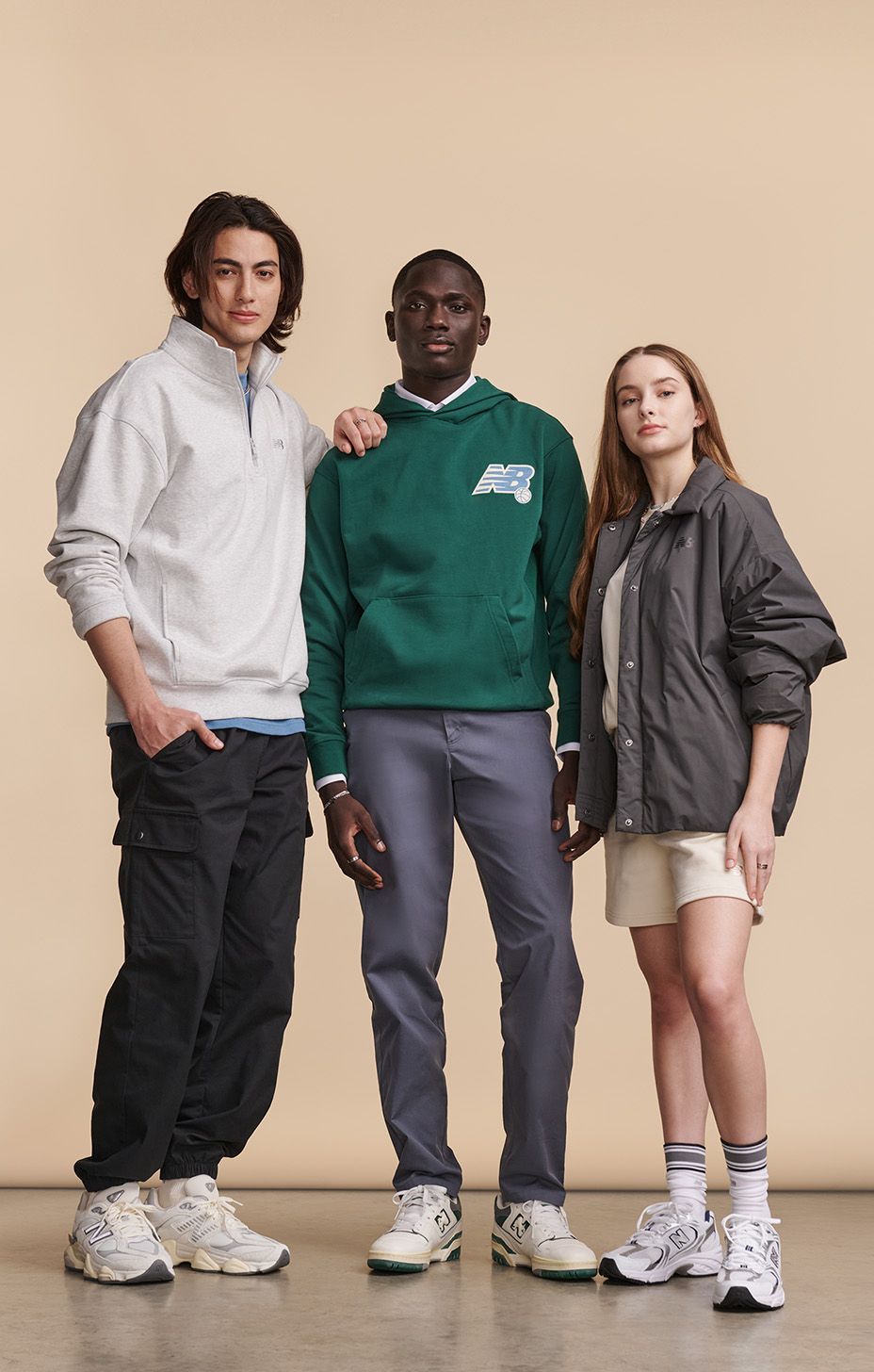 Grupa mężczyzn i kobiet ubranych w odzież i buty New Balance, pozująca na beżowym tle w studio.