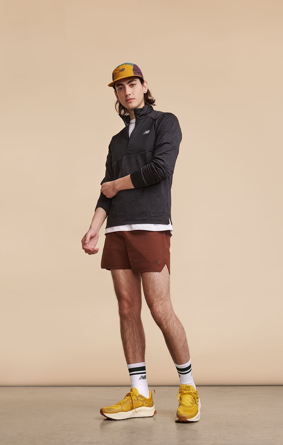 Mężczyzna ubrany w odzież i buty do biegania New Balance, pozujący na beżowym tle w studio.